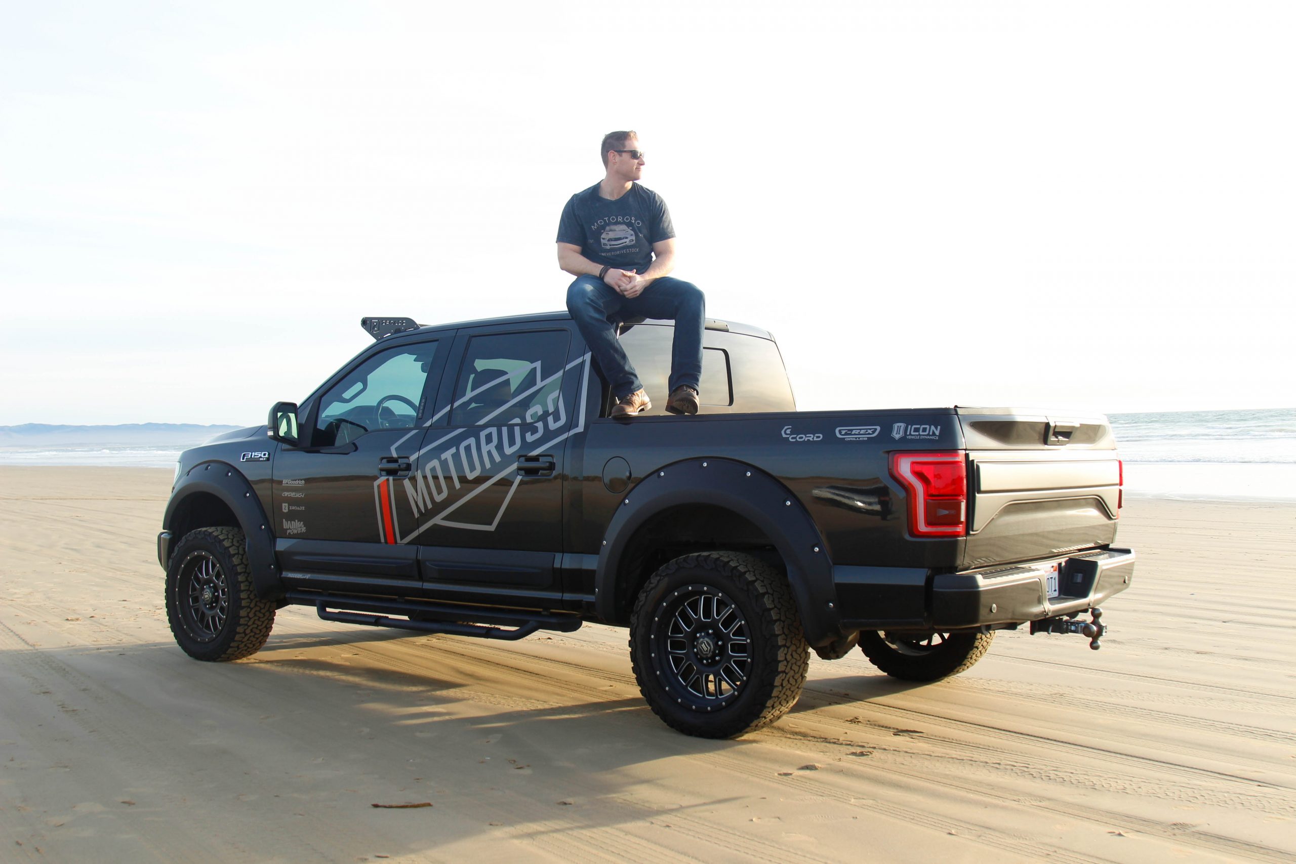 Founder of Motoroso sitting on the roof of his black pickup truck on the beach.