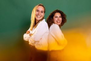 Co-founders of Cheekies McCall Brinskele and Mariana Inofuentes standing back to back with their arms crossed, in front of a green backdrop.